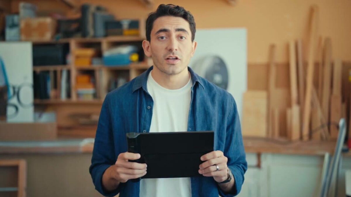 Ein Mann in einer Werkstatt hält ein flaches schwarzes Gerät in Tabletgröße in beiden Händen